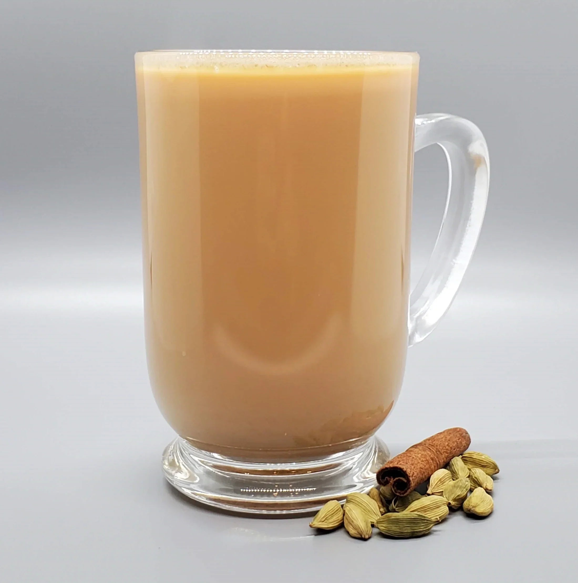 Leely Chai Co. creamy masala chai in a clear glass mug with whole cinnamon stick and green cardamom pods beside it.