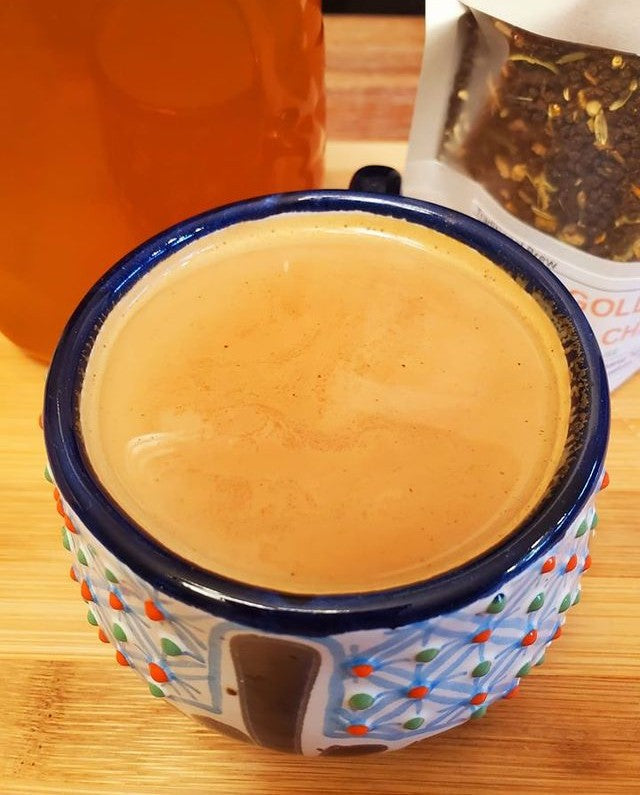 Freshly brewed masala chai in a handcrafted ceramic mug with tea leaves and brewed tea in the background.