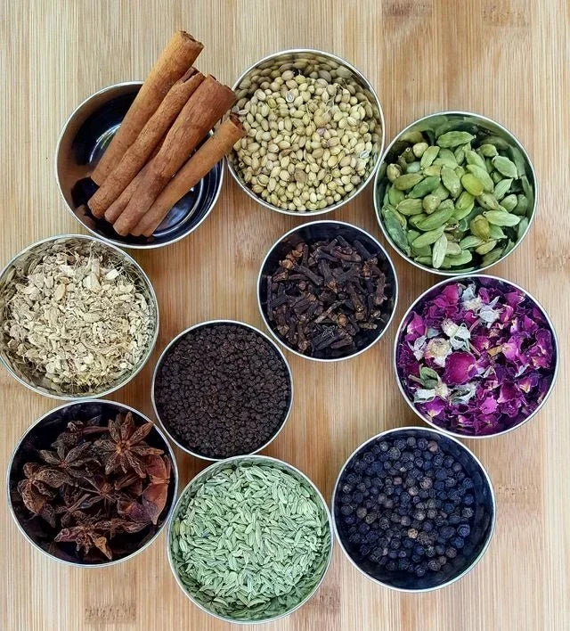 Leely Chai Co. whole chai spices arranged in bowls, including cloves, cinnamon, cardamom, fennel, peppercorns, and rose petals.