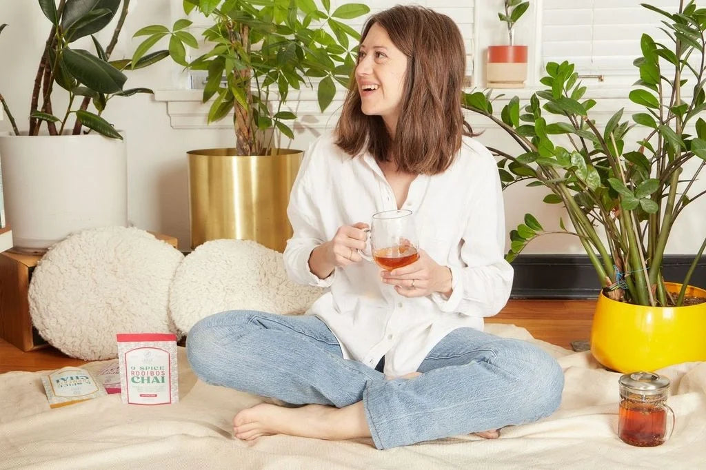 Woman enjoying a relaxing morning with Leely Rooibos Chai, surrounded by houseplants in a bright, cozy living space.